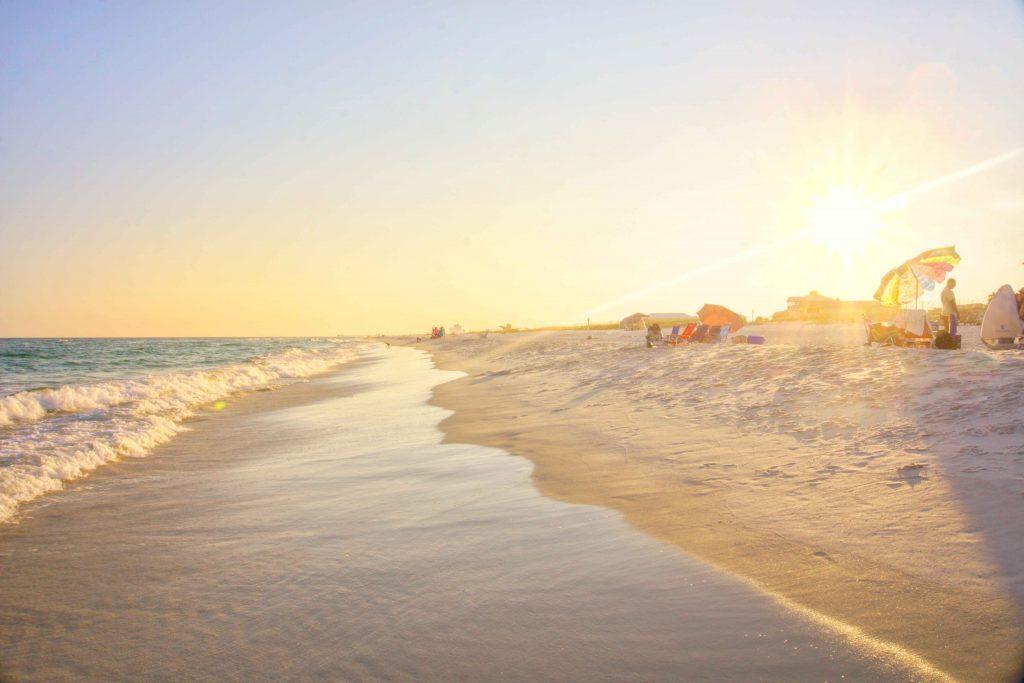 Image of a beach with the sea rolling into the sand and the low sun in the background