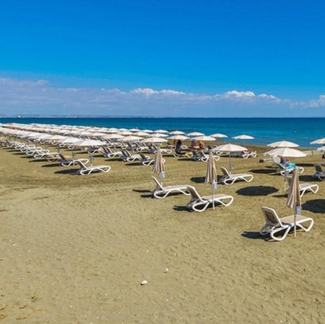Rows of sunbeds and parasols lining the sea's edge on a sandy beach, facing the Mediterranean Sea - Larnaca Mackenzie beach, Cyprus.