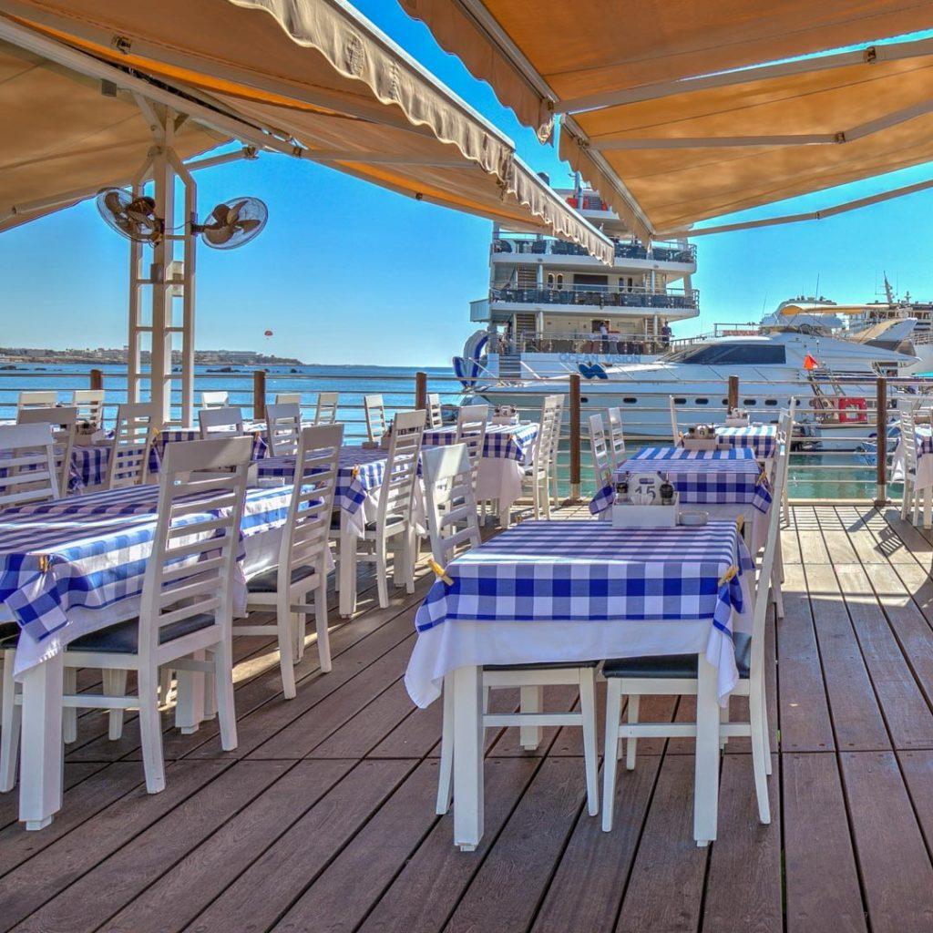 View of restaurant tables with checked table clothes, on Paphos Harbour. Presented by Comark Estates.