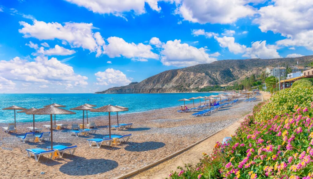 Photo of Pissouri Bay beach, showing blue sunbeds, parasols, cliffs in the background and the Mediterranean Sea